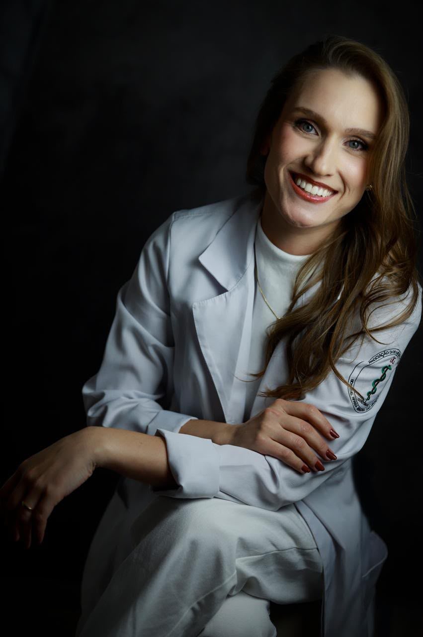 Dra. Sarah de Lázari de jaleco, sorrindo, em fundo escuro